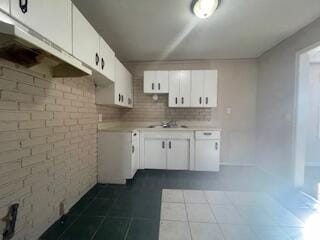 kitchen featuring white cabinets, tasteful backsplash, dark tile patterned floors, and brick wall