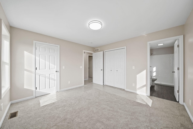 unfurnished bedroom featuring carpet, two closets, and ensuite bathroom