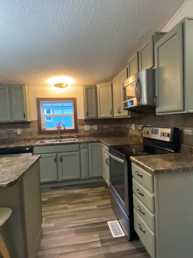 kitchen featuring a textured ceiling, dark hardwood / wood-style floors, stainless steel appliances, sink, and green cabinetry