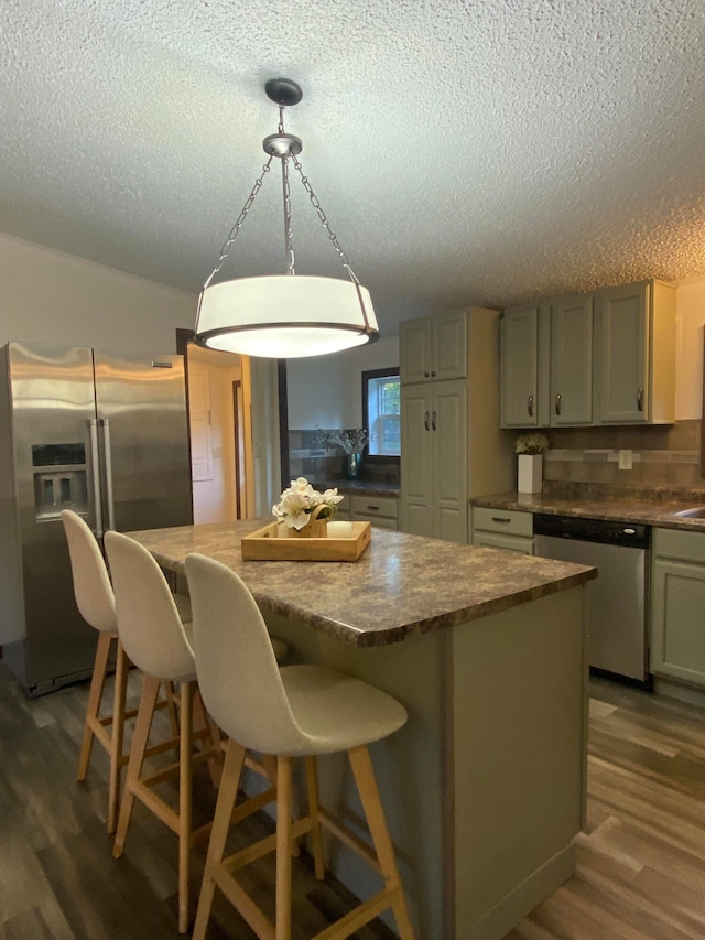 kitchen with a textured ceiling, hardwood / wood-style flooring, stainless steel appliances, and a breakfast bar area