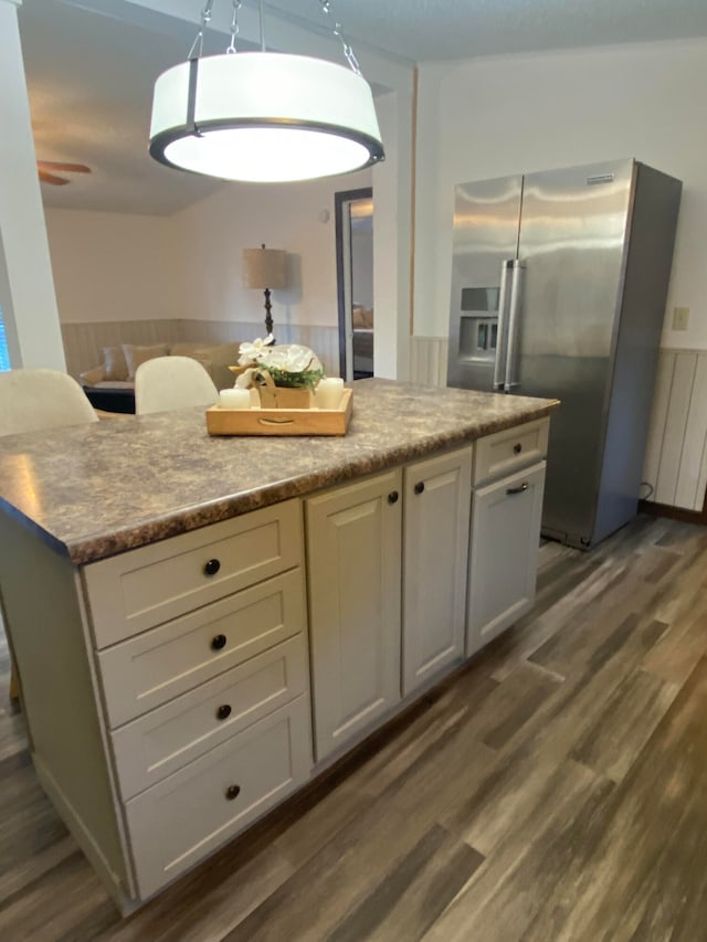 kitchen featuring light stone countertops, hanging light fixtures, stainless steel fridge, white cabinets, and dark wood-type flooring