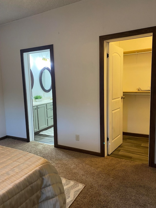 bedroom with a spacious closet, ensuite bath, a textured ceiling, and dark carpet