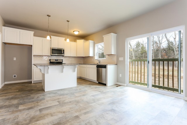 kitchen featuring appliances with stainless steel finishes, white cabinets, light stone countertops, a center island, and decorative light fixtures