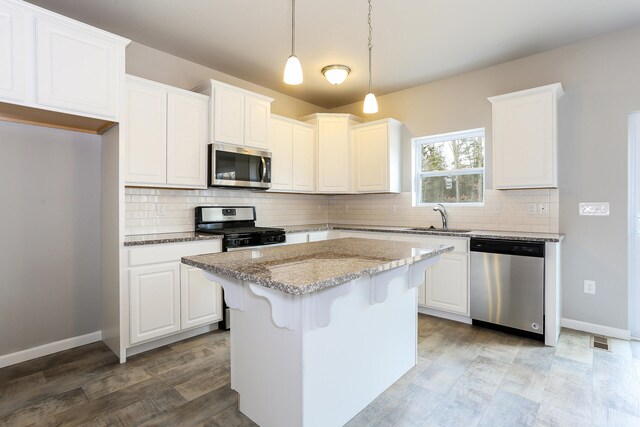 kitchen with light stone counters, a center island, stainless steel appliances, and white cabinets