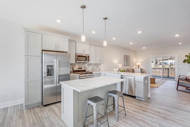 kitchen featuring sink, kitchen peninsula, light hardwood / wood-style flooring, stainless steel appliances, and decorative light fixtures