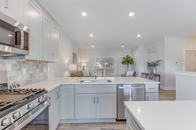 kitchen featuring light stone counters, sink, kitchen peninsula, light hardwood / wood-style flooring, and appliances with stainless steel finishes