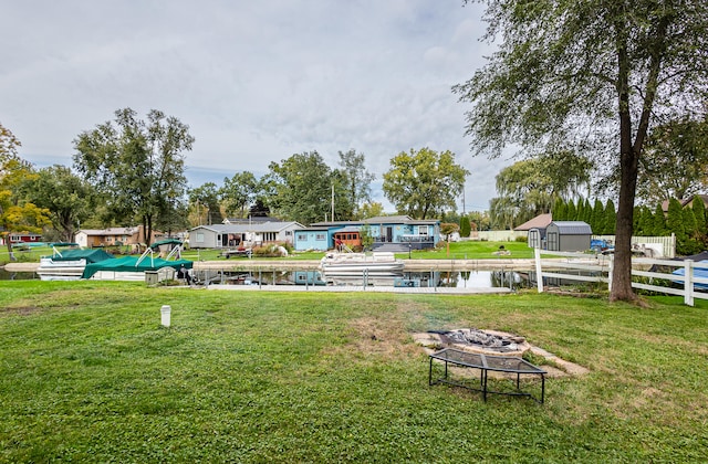 view of community featuring a storage shed, a water view, an outdoor fire pit, and a yard