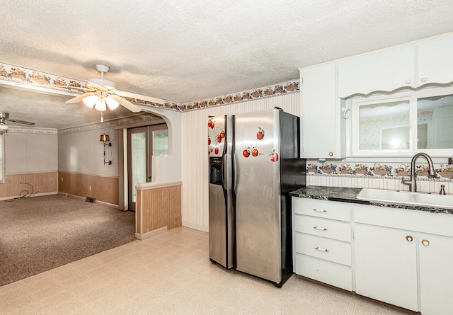 kitchen featuring white cabinets, sink, a textured ceiling, wooden walls, and stainless steel fridge with ice dispenser