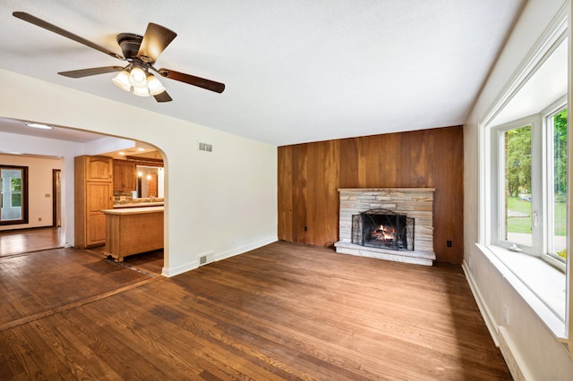 unfurnished living room with ceiling fan, a fireplace, wood walls, and hardwood / wood-style floors