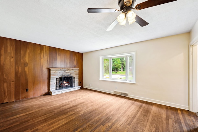 unfurnished living room with ceiling fan, hardwood / wood-style floors, a fireplace, wood walls, and a textured ceiling