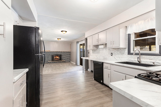 kitchen featuring white cabinets, tasteful backsplash, light hardwood / wood-style flooring, black appliances, and sink