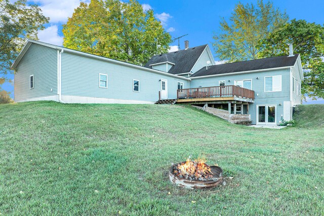 rear view of property with a lawn, a deck, and a fire pit