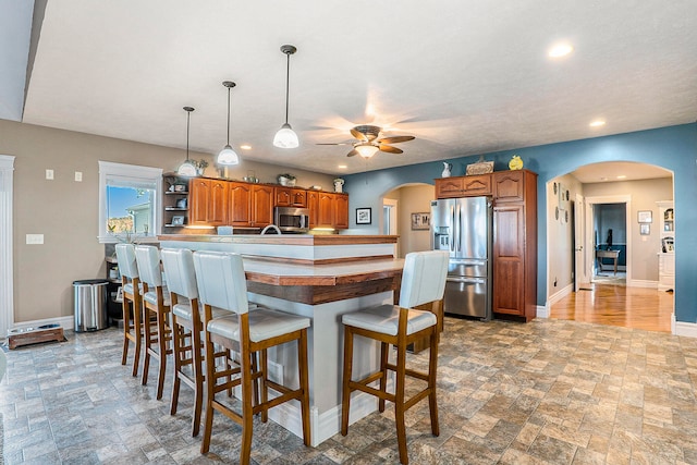 kitchen featuring a breakfast bar, pendant lighting, kitchen peninsula, appliances with stainless steel finishes, and ceiling fan