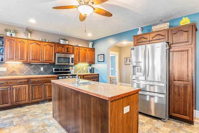 kitchen with appliances with stainless steel finishes, backsplash, sink, and an island with sink