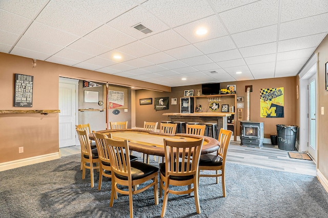 dining space featuring wood-type flooring, a wood stove, and a paneled ceiling