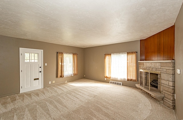 unfurnished living room with wooden walls, a textured ceiling, light colored carpet, and a fireplace