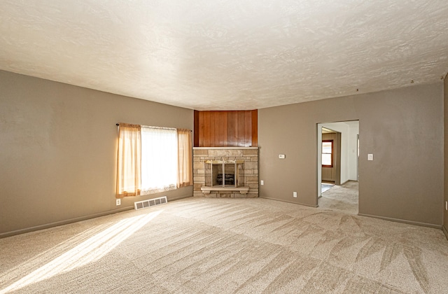 unfurnished living room with light colored carpet, a textured ceiling, and a fireplace