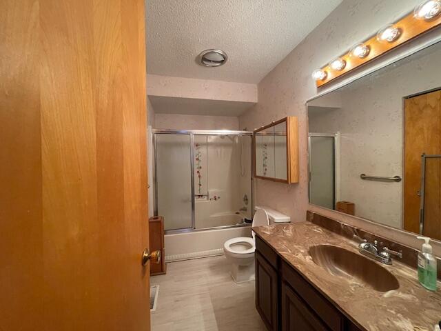 full bathroom with vanity, enclosed tub / shower combo, a textured ceiling, and toilet