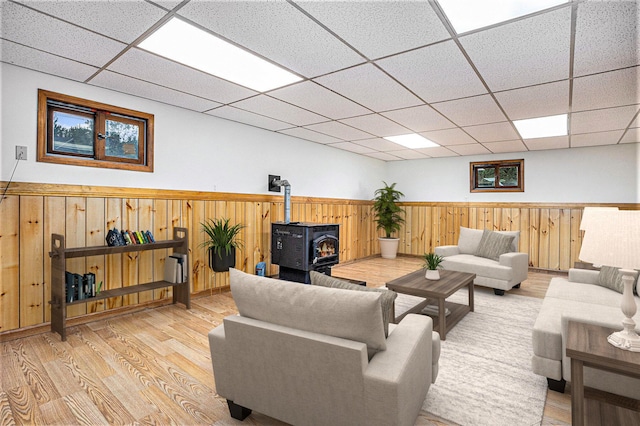 living room with a paneled ceiling, wood walls, light wood-type flooring, and a wood stove