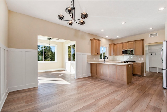 kitchen featuring light wood-type flooring, decorative light fixtures, decorative backsplash, kitchen peninsula, and appliances with stainless steel finishes