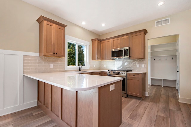 kitchen with sink, stainless steel appliances, light wood-type flooring, and kitchen peninsula