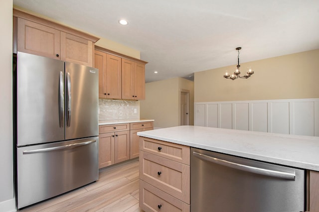 kitchen with appliances with stainless steel finishes, light brown cabinetry, an inviting chandelier, and light hardwood / wood-style flooring