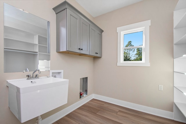 washroom with hookup for a washing machine, sink, light hardwood / wood-style floors, and cabinets