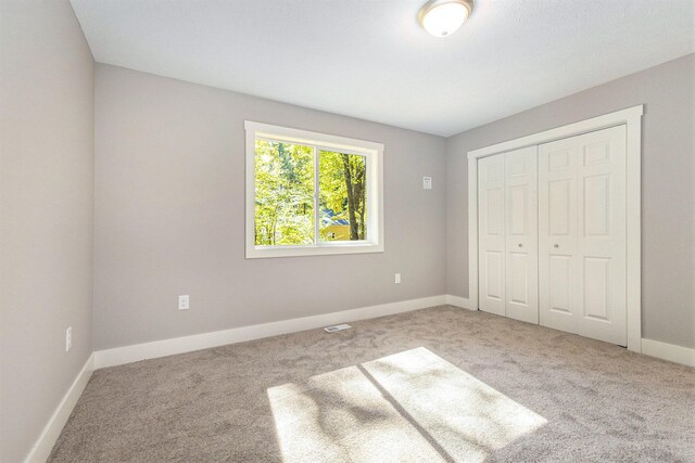 unfurnished bedroom with light colored carpet and a closet