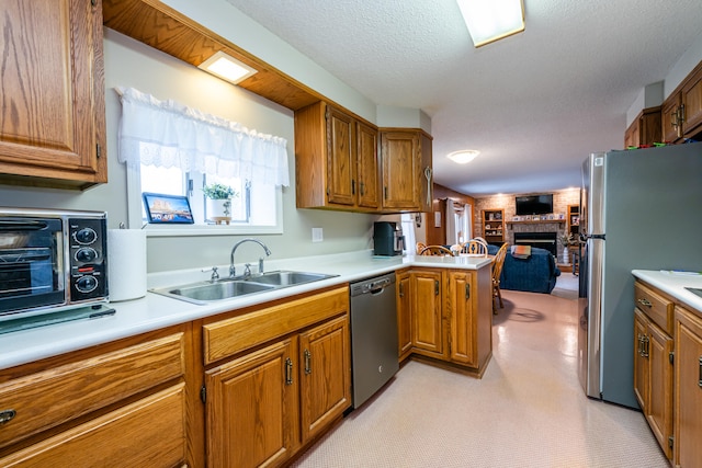 kitchen featuring appliances with stainless steel finishes, a fireplace, kitchen peninsula, a textured ceiling, and sink