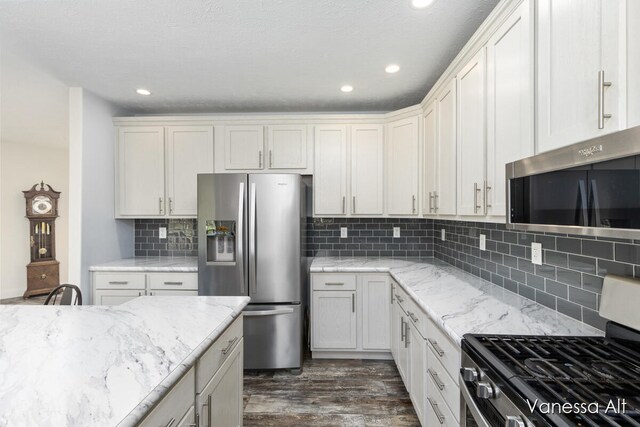 kitchen with stainless steel appliances, white cabinetry, backsplash, and light stone countertops