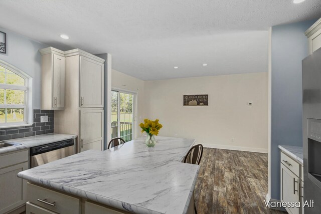 kitchen with light stone countertops, stainless steel dishwasher, tasteful backsplash, a kitchen island, and dark hardwood / wood-style flooring