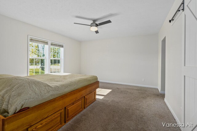 carpeted bedroom featuring a textured ceiling, ceiling fan, and a barn door