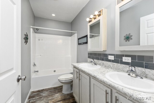 full bathroom featuring toilet, hardwood / wood-style floors, decorative backsplash, shower / washtub combination, and vanity