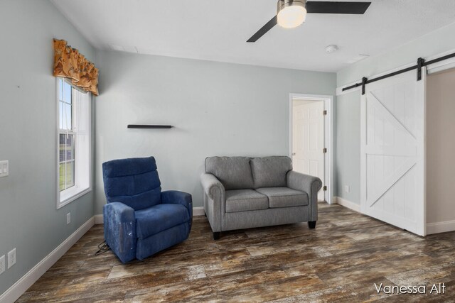 living area with ceiling fan, a barn door, and dark hardwood / wood-style floors