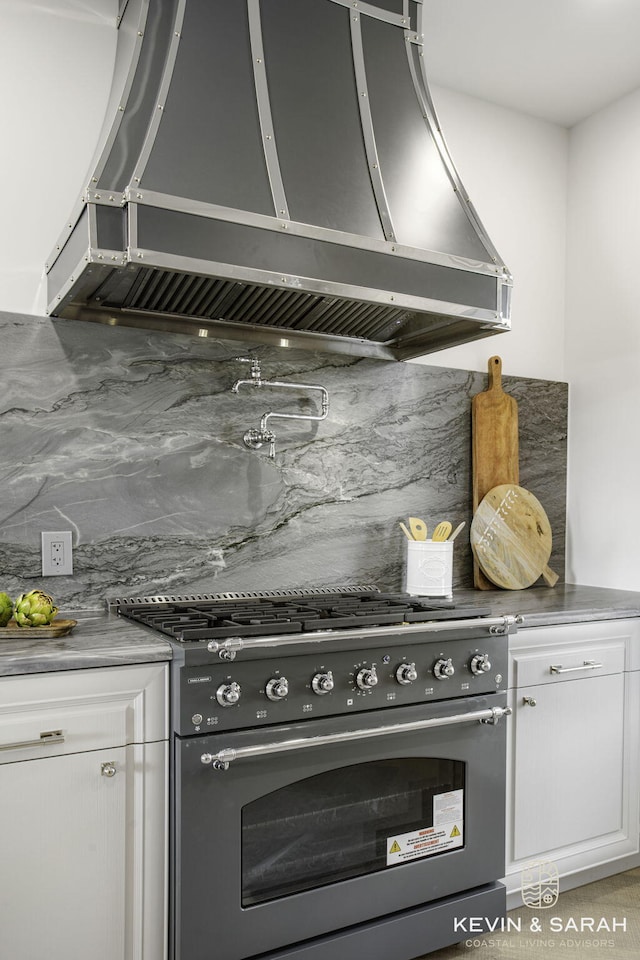 kitchen with decorative backsplash, wall chimney exhaust hood, white cabinetry, and high end stove