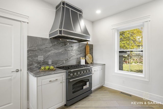 kitchen with high end range, light hardwood / wood-style floors, custom exhaust hood, white cabinets, and decorative backsplash