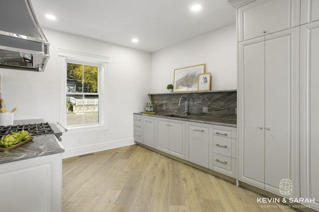 bar with range hood, white cabinetry, sink, and light wood-type flooring