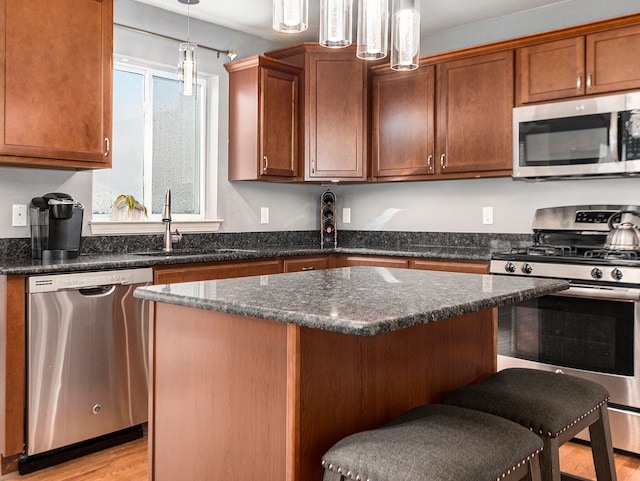 kitchen with sink, light hardwood / wood-style flooring, decorative light fixtures, a breakfast bar area, and appliances with stainless steel finishes