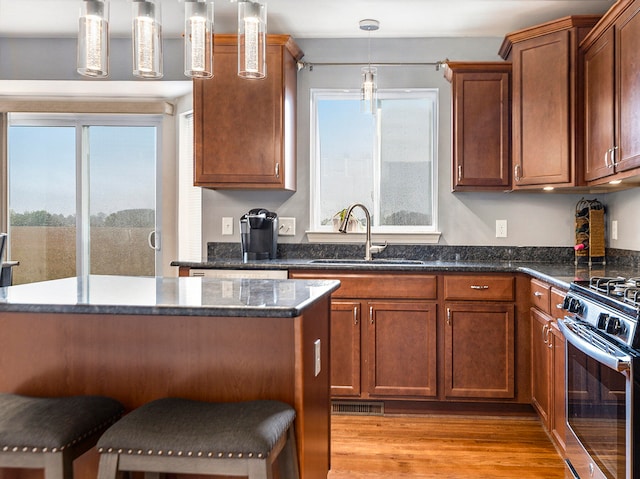 kitchen with gas stove, sink, light hardwood / wood-style flooring, decorative light fixtures, and a breakfast bar area