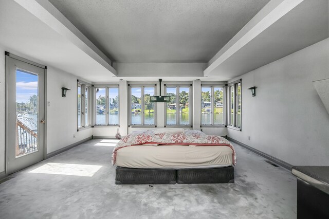 bedroom featuring a water view, a textured ceiling, a raised ceiling, and access to outside