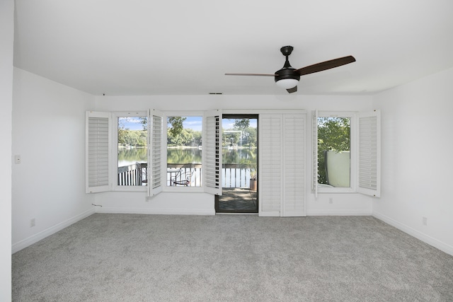 spare room with light carpet, a water view, and ceiling fan