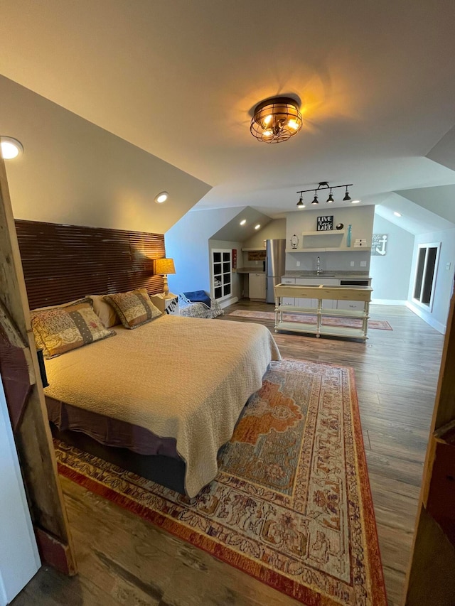 bedroom with stainless steel refrigerator, vaulted ceiling, hardwood / wood-style floors, and sink