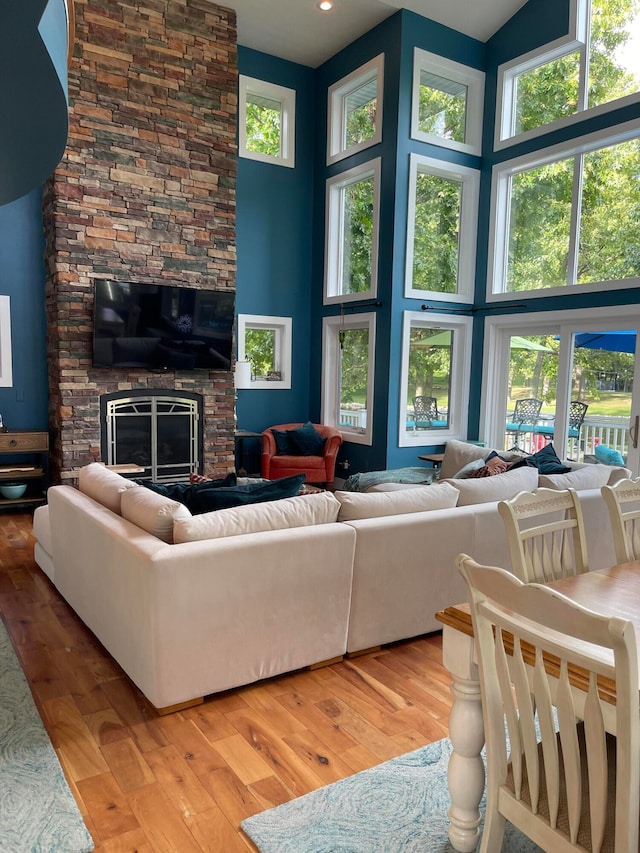 living room featuring a stone fireplace, light hardwood / wood-style floors, plenty of natural light, and a high ceiling