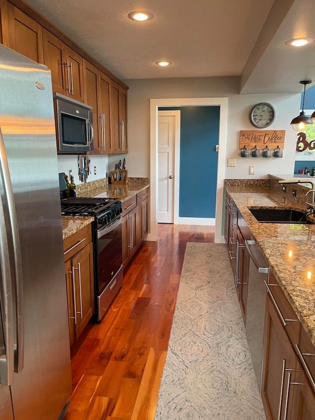 kitchen with dark wood-type flooring, sink, appliances with stainless steel finishes, decorative light fixtures, and light stone countertops