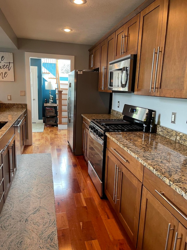 kitchen featuring stainless steel appliances, a textured ceiling, stone countertops, and dark wood-type flooring