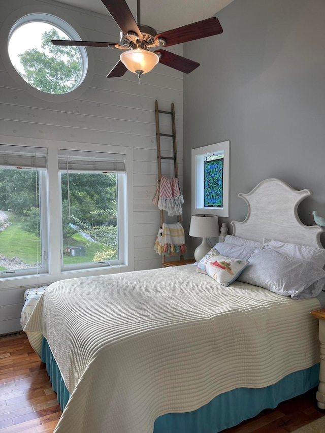 bedroom featuring ceiling fan, multiple windows, hardwood / wood-style floors, and wooden walls