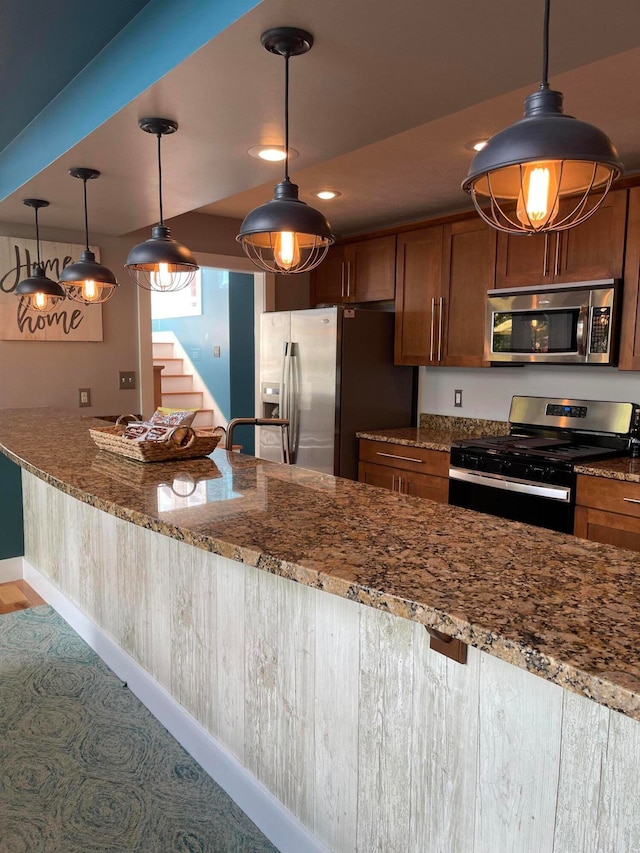 kitchen with light stone counters, decorative light fixtures, and stainless steel appliances