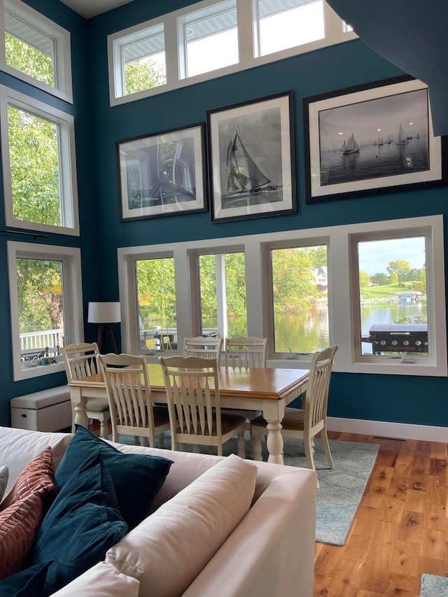 dining space with a towering ceiling, a water view, hardwood / wood-style flooring, and plenty of natural light