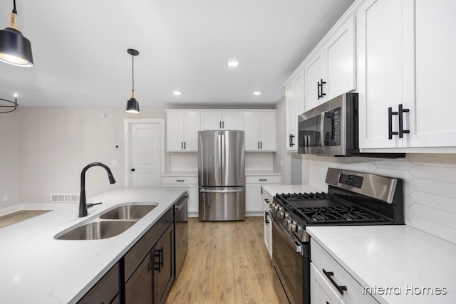 kitchen featuring white cabinets, appliances with stainless steel finishes, decorative light fixtures, and sink