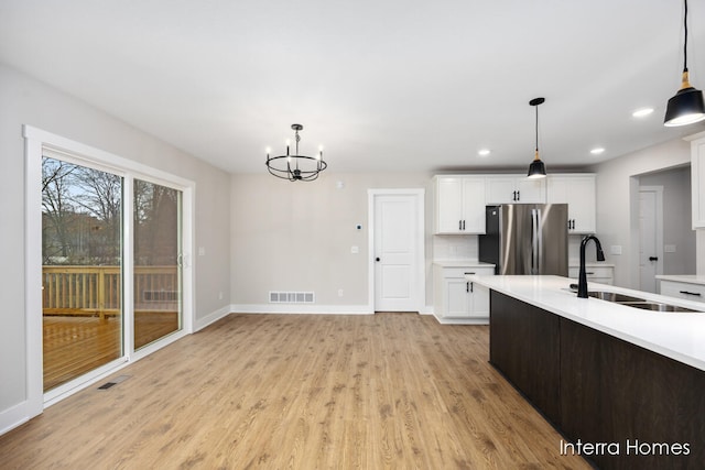 kitchen featuring sink, hanging light fixtures, stainless steel fridge, light wood-type flooring, and white cabinetry